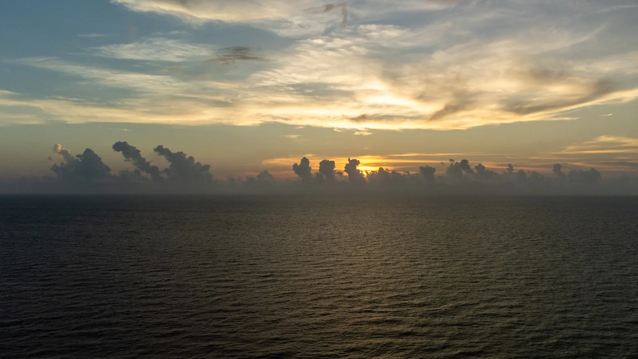 The setting sun breaks through layered clouds over the Gulf.